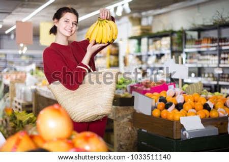 Portrait of happy brunette girl buying ripe bananas in supermarket 