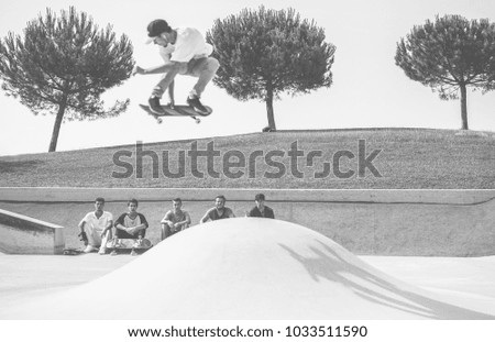 Blurred young skater jumping with skateboard while friends watching him - Sporty guy performing tricks and skills  - Extreme sport, youth lifestyle concept - Focus on trees - Black and white editing