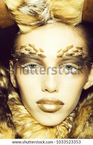 Closeup portrait of one beautiful wild young woman with bright golden animal monkey makeup with thorns on face in fur coat in studio, vertical picture