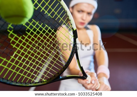 Portrait of forceful woman playing tennis in indoor court, focus on tennis racket hitting ball, copy space