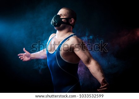 A strong dark-haired sportman  in a blue wrestling tights and training mask posing  against a blue and red vape smoke background on a black isolated 