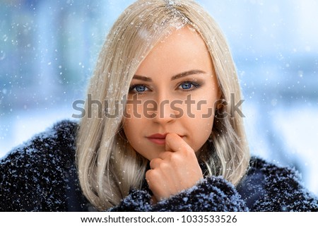 Winter portrait of smiling beautiful blonde girl under the hard snow - close-up beauty photo.