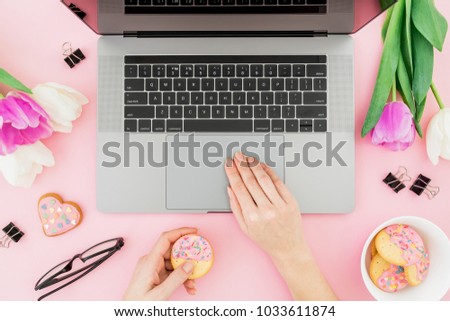Woman working with computer. Office desk with laptop, tulip flowers, glasses, pen and cookies on pink background. Flat lay. Top view.