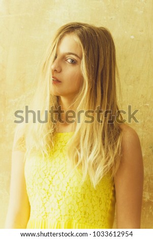 Pretty girl or cute woman with long blond hair and adorable happy face in yellow dress on textured wall background