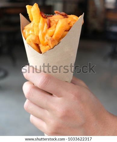 Hand holds Delicious french fries topping with cheddar cheese cream and crispy bacon.  Royalty-Free Stock Photo #1033622317