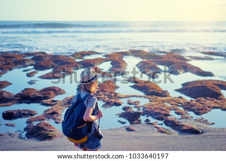 Traveling and photography. Young woman with camera and backpack walking by sea beach.