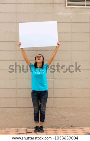 Portrait of young woman holding blank white board on brick wall background