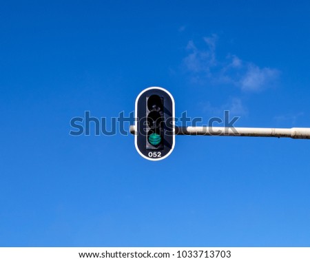 Green traffic light on a horizontal white metal beam, against a blue sky
