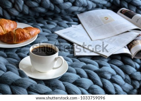 A cup of coffee, croissants and magazines on a knitted plaid