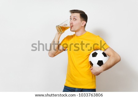 Inspired young fun cheerful European man, fan or player in yellow uniform drink pint mug of beer, soccer ball cheer favorite football team isolated on white background. Sport, play, lifestyle concept