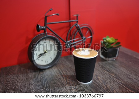 A cup of fragrant and beautiful coffee stands on a table on the background of a red wall and a small figure bicycle. Picture on foam - leaf