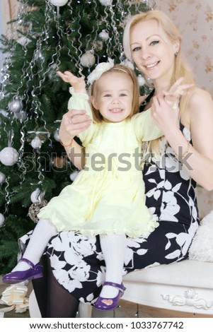 Cheerful mom and cute baby girl against the background of Christmas decorations.