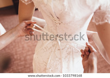 The girlfriend helps the bride to lace a beautiful wedding dress with lace tying a bow.