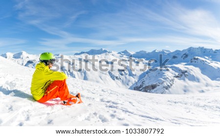 Image of sportive man wearing helmet wearing yellow jacket sitting on snowy slope during day