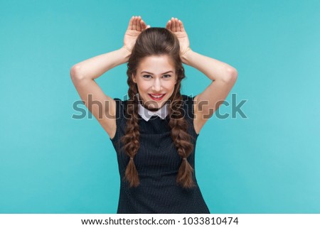 Funny young woman showing rabbit sign and smile. Indoor, studio shot on blue background