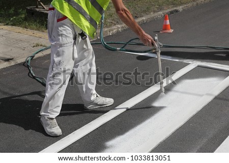 Worker spraying pedestrian crosswalk at a street,  repairing and painting