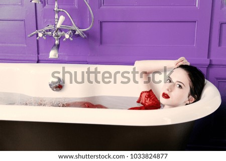 portrait of beautiful young woman lying in bath full of flowers and foam and relaxing