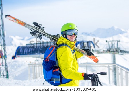 Photo of sporty man wearing helmet with skis on his shoulder against backdrop of funicular