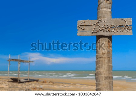 Beach sign made from manila rope on old wooden board and coconut pole with blurred cottage on the beach and clear blue sky background, Copy space and selective focus