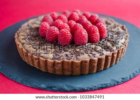 Chocolate tartlet with raspberry on black board on red background