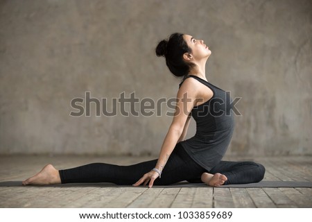 Young woman practicing yoga, doing Single Pigeon, Eka Pada Raja Kapotasana exercise, One Legged King Pigeon pose, working out, wearing sportswear, indoor full length, gray wall in yoga studio Royalty-Free Stock Photo #1033859689