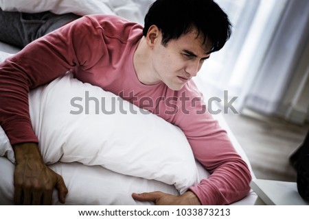 Frustation caucasian male wake up in morning while alarm clock. Sad depressed man suffering from insomnia, he is lying in bed and touching his forhead,sleep disorder and stress concept. 