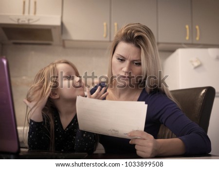 Worried mother sitting at table with bills and laptop while her daughter sitting next to her.