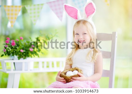 Cute little girl wearing bunny ears playing egg hunt on Easter. Adorable child celebrate Easter at home.