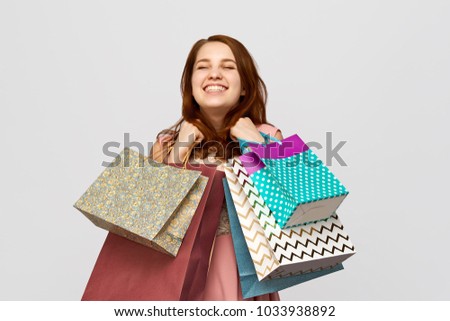Portrait of happy joyful young woman with long red hair, pleased that she bought everyone gifts for the holidays. Shopaholic girl stands on isolated white background with lots of packages.