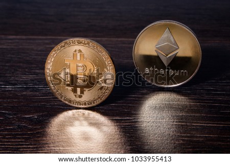 Golden Bitcoin and ethereum crypto currency physical real metal coins reflected on a dark wooden surface.