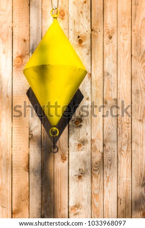 Buoy, yellow, cone-shaped hangs as a decoration in front of board wall of different widths vertical light wooden boards with natural grain