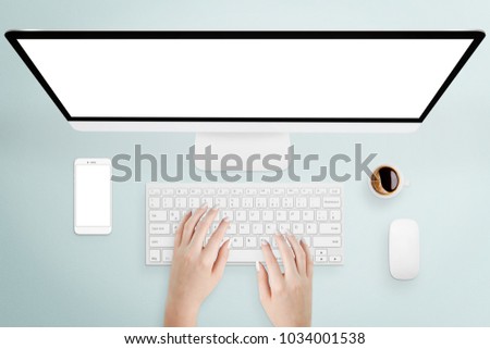 Female hands typing on keyboard of desktop computer with isolated screen, surrounded with smartphone and coffee on light blue desk, top view. Mock-up, free space for text, icons, etc