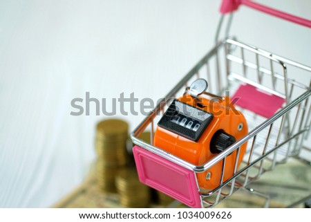 Tally counter or counting machine with 0000 number and shopping cart or supermarket trolley on white wooden table, business and finance concept idea.