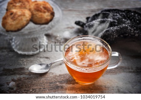 hot tea with steam in a glass cup on a wooden table, cookies and snowy gloves blurred in the background, best warm up after a winter walk, selected focus, narrow depth of field