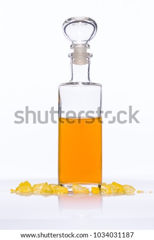 Bright glass bottle filled with an orange liquid in front of a white background, surrounded by glass stones