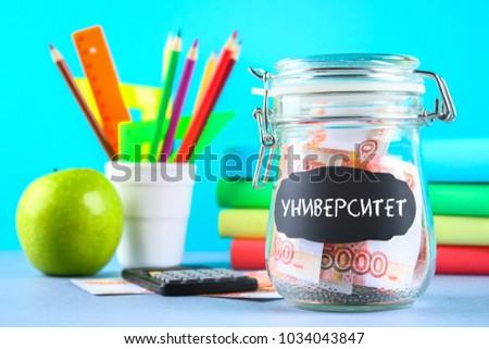 Bank with Russian money, 5000 rubles and a calculator, books on a gray background. Finance, moneybox, education. Text in Russian: university