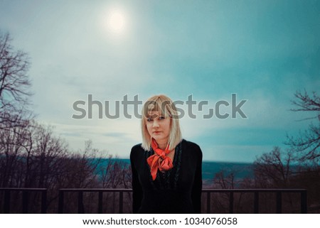 Blonde woman with red scarf and black shirt in the forest looking at the camera. Springtime, outdoor portrait.