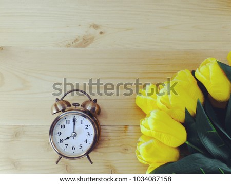 alarm clock on wooden background with artificial tulip bouquet and space copy
