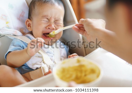 6 months old Asian baby refuse to eat food and crying over feeding time, Royalty-Free Stock Photo #1034111398