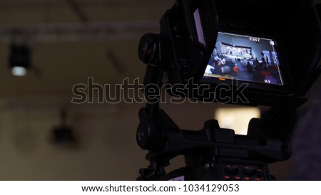 Behind the scene of tv movie video film shooting production crew team and camera lighting set in the big studio. Professional digital video camera in studio. Cameraman working with announcer in