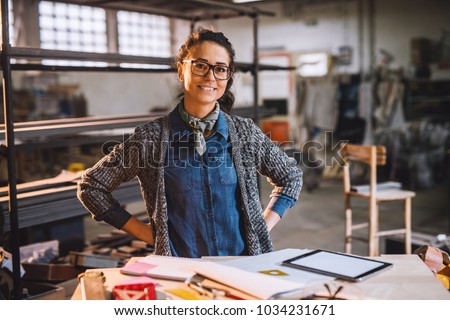 Portrait of cheerful happy middle aged engineer in sunny fabric workshop and posing behind the desk with tools.