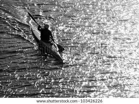 Silhouette of a man kayaking in the lake at sunset. Classical black and white photography of high contrast scene.