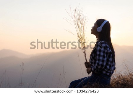 young  asian woman wear listening to music  headphones on the Moutain Sunset Background
