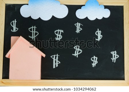 Toy house with toy cloud 'raining' money sign on blackboard. Conceptual.