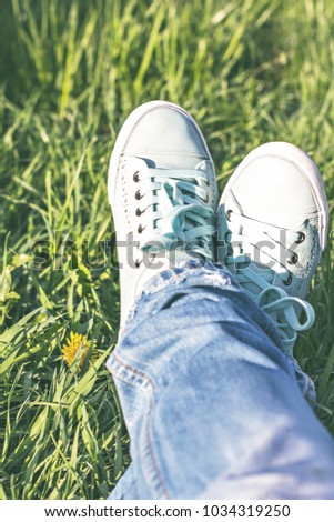 Female legs in a clearing with green grass. Blue sneakers. Spring Park, spring walk.