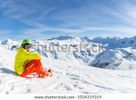 Image of sportive man wearing helmet wearing yellow jacket sitting on snowy slope