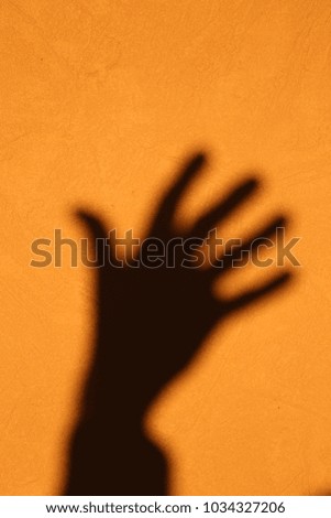 Close up interior view of a human arm silhouette. Shadow of a hand and a arm drawn on a beige wall by the sun. Dark isolated shape with five fingers. Abstract strange design with part of a human body