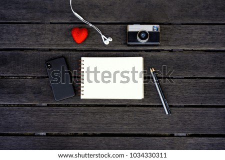 Minimal styled flat lay isolated on dark wood background. Man desk top view with summer accessories: heart, smartphone, vintage photo camera, headphones, coffee, notebook. Woman's day postcard