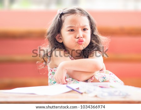 Angry little cute 
girl with cross one's arm.The emotion of a child when her mother forbids watching cartoons and tell her to draw.