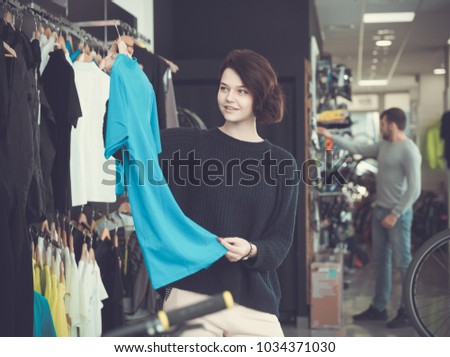 Young woman choosing sport shirt in bicycle shop
